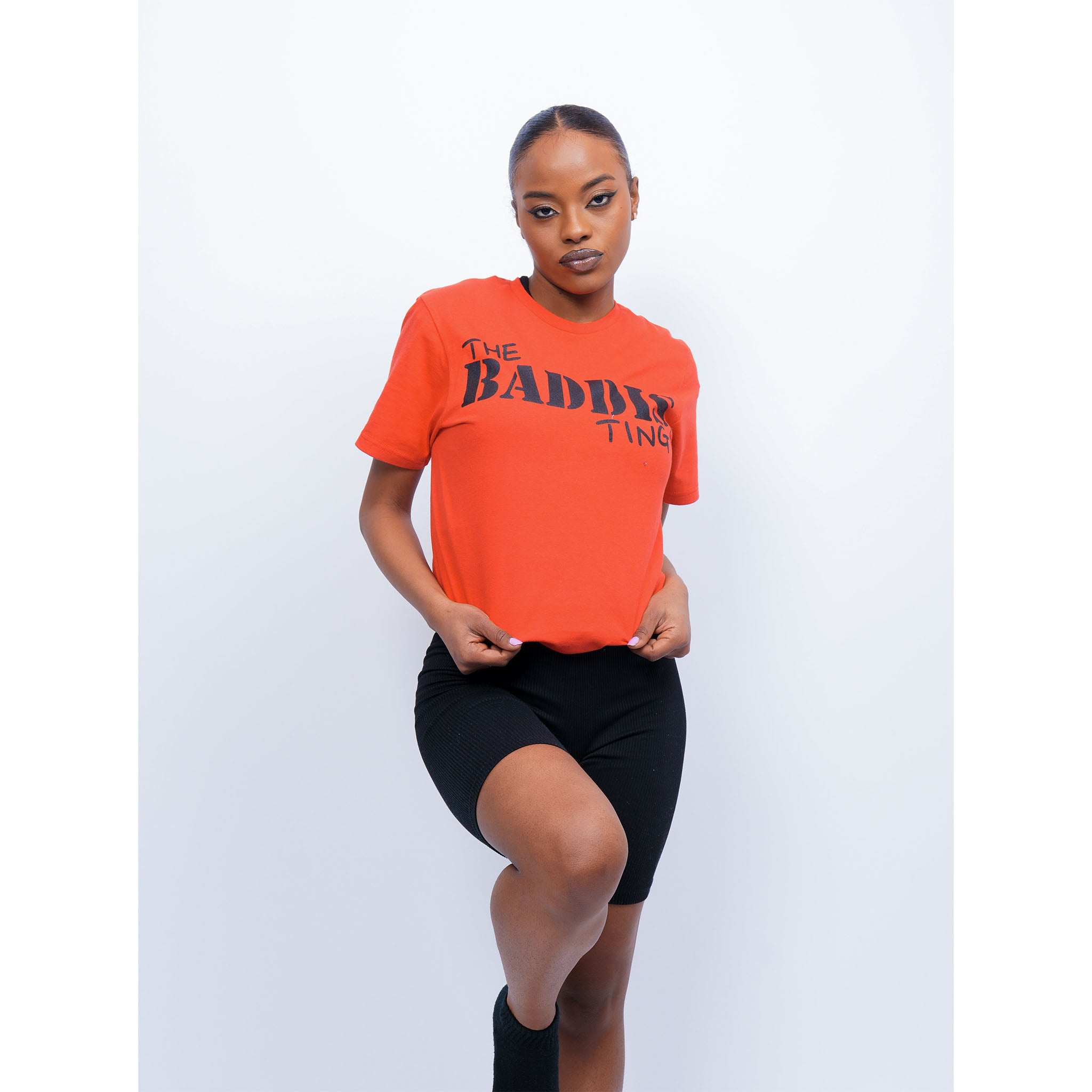 Female model is wearing The Baddis Ting Red T Shirt, folded to give a crop top look.
